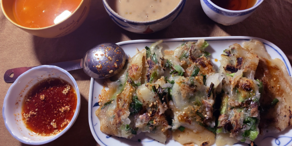 画像右下から時計回りにチヂミ・胡麻が浮いたチヂミのタレ・具が見えないけれどキムチ仕立てのお味噌汁・実が見えないけれど緑豆ぜんざいココナッツミルク仕立て・お茶。